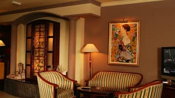 Een hotel lobby met een groot raam, twee gestreepte fauteuils, een kleine tafel, een lamp, een schilderij en een televisie.