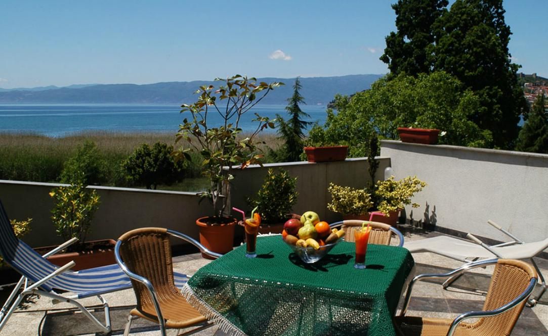 A terrace with a table set for two, a view of the sea, and potted plants.