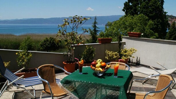 A terrace with a table set for two, a view of the sea, and potted plants. - Millenium Palace (Ohrid)