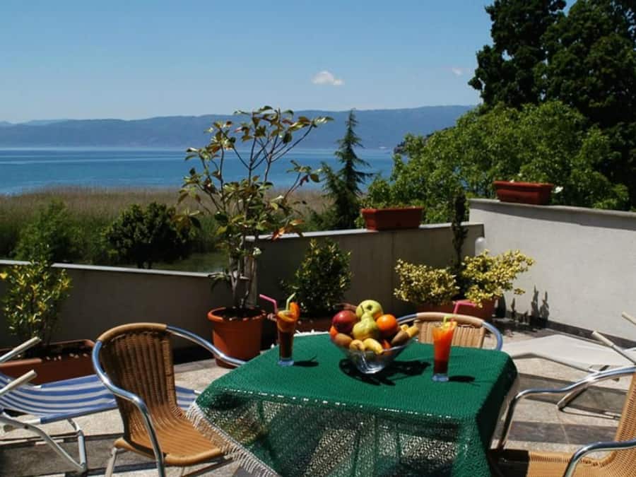 En terrasse med et bord dækket til to, havudsigt og plantekasser.