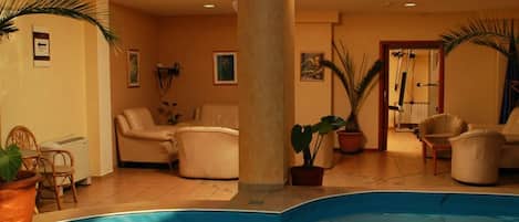 A pool area with a large column, lounge chairs, and potted plants.