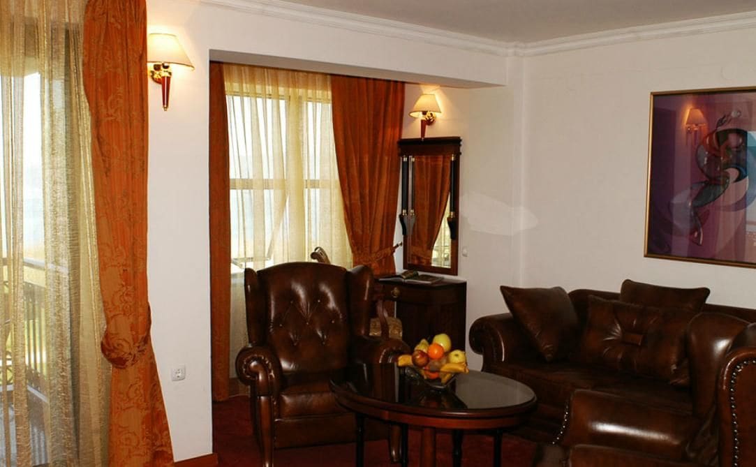 A room with a leather sofa, a wooden coffee table with fruit, a chair, and a painting on the wall.
