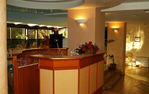 A bar area with a wooden counter, bar stools, and a potted plant with red flowers. - Millenium Palace (Ohrid)