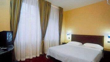 A hotel room with a bed, curtains, a desk, and a television.