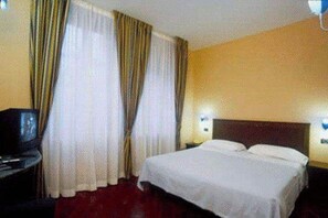 Una habitación de hotel con cama, cortinas, escritorio y televisor.