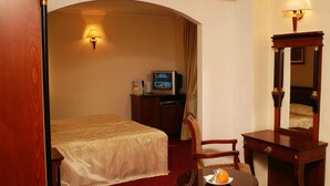 A hotel room with a bed, a desk, a chair, a television, and a lamp. - Millenium Palace (Ohrid)