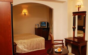A hotel room with a bed, a desk, a chair, a television, and a lamp. - Millenium Palace (Ohrid)