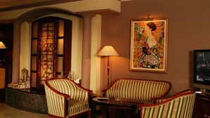 A hotel lobby with striped armchairs, a large painting, and a television.