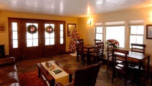 A dining area with a wooden table, chairs, and a Christmas tree. There are two doors with wreaths and a window with a view. - BackCountry Inn (Norwood)