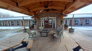 An outdoor patio area with stone flooring, wooden tables and chairs, and potted plants. - BackCountry Inn (Norwood)