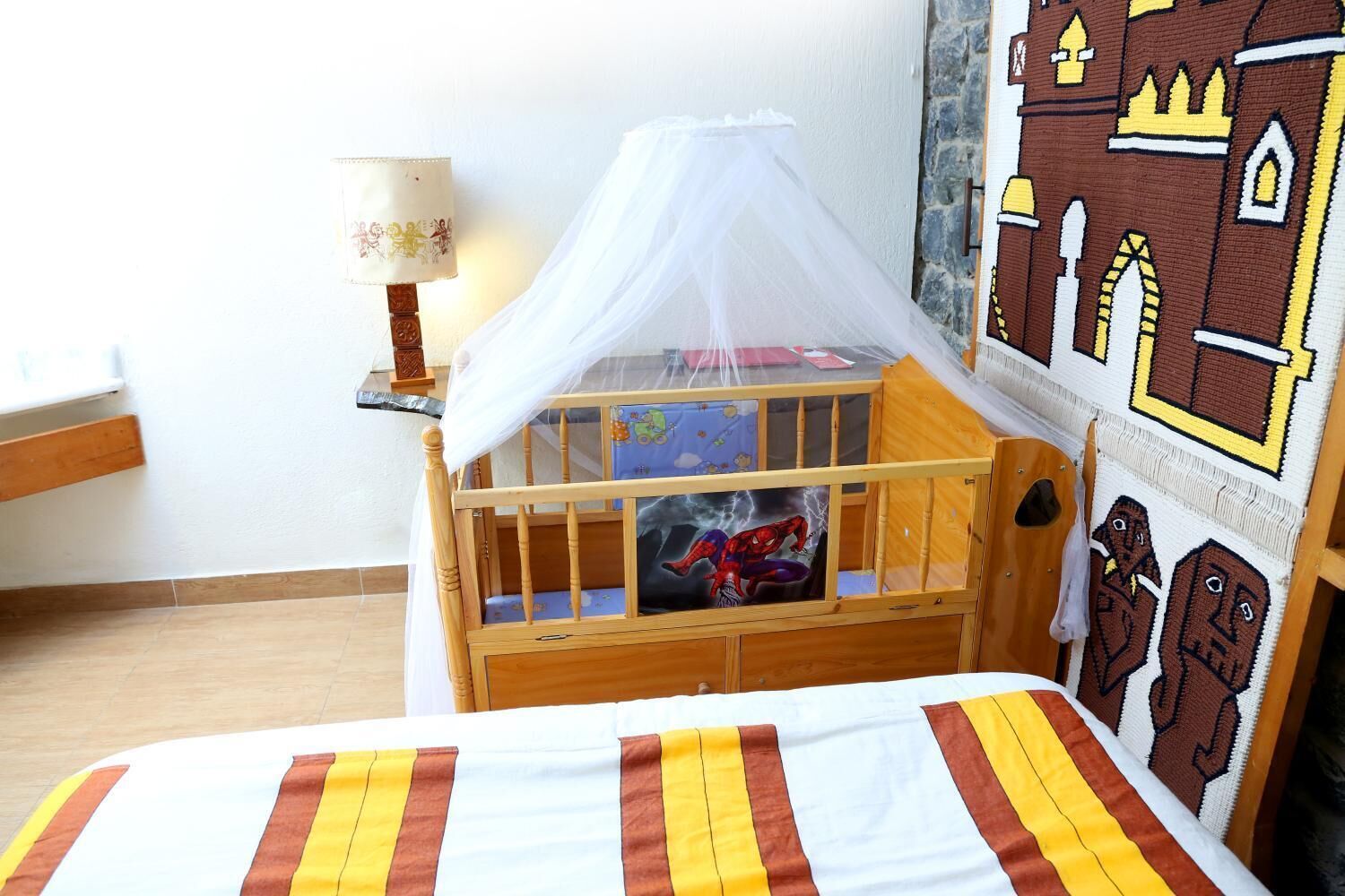 A child's wooden bunk bed with a mosquito net, a bedside table with a lamp, and a wall mural.