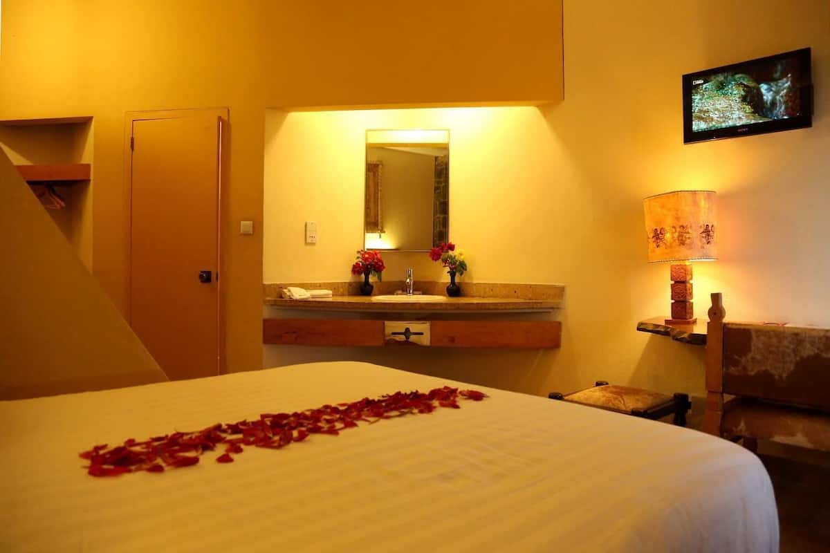 A hotel room with a bed, a bathroom with a sink and mirror, a TV on the wall, and a lamp.