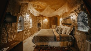 A stone-walled bedroom with a bed, a nightstand, a lamp, and a television. - Dere Suites (Ürgüp)