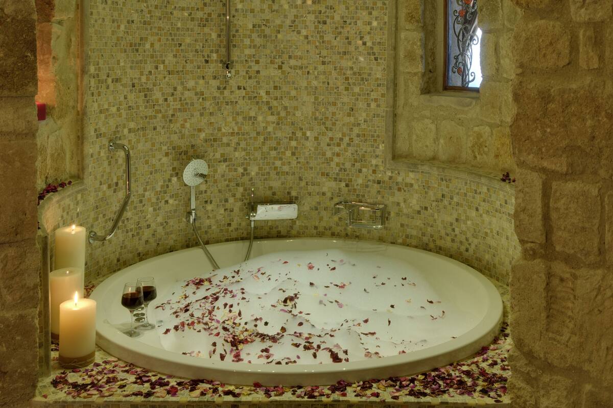 Una bañera con pétalos de rosa y velas, rodeada de mosaicos.