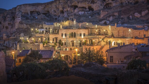 A historic town with stone buildings and a prominent cliff with cave dwellings. - Dere Suites (Ürgüp)