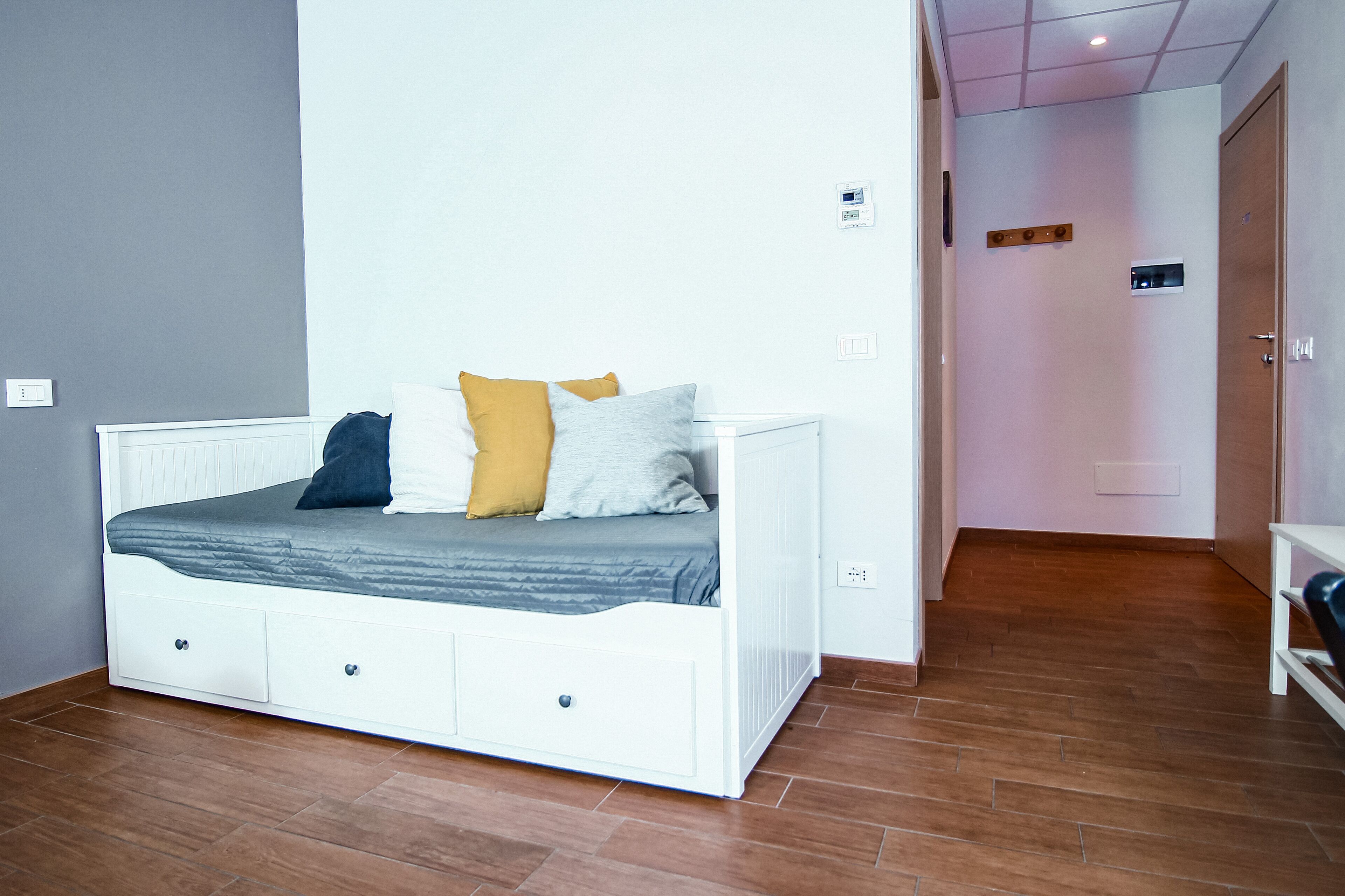 Een slaapkamer met een wit bed, houten vloeren en een deur naar een andere kamer.