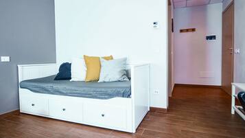 Een slaapkamer met een wit bed, houten vloeren en een deur naar een andere kamer.