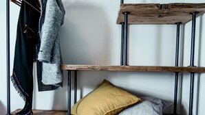 A multi-tiered wooden shelf unit with metal legs, holding various items including a coat, a scarf, and pillows. - Agriturismo Il Cucchiaio di Legno (Orta San Giulio)