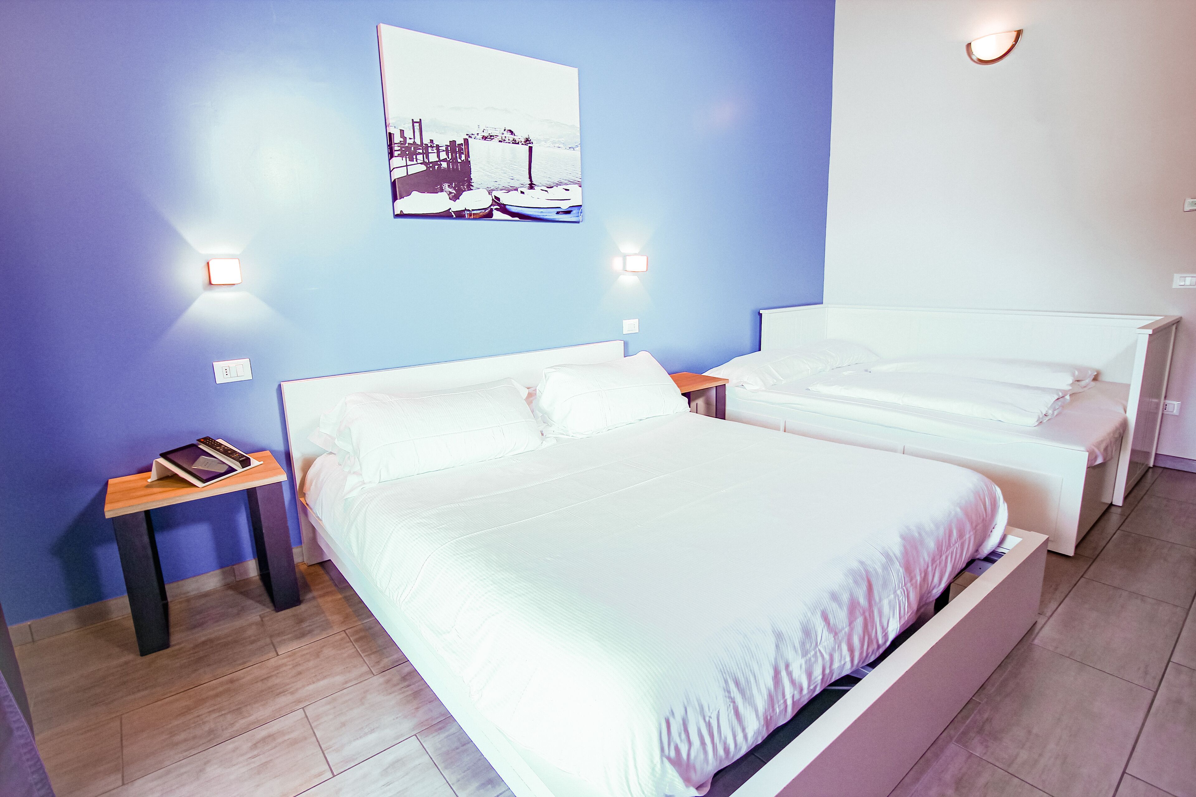 Habitación de hotel con dos camas, una mesita de noche, una lámpara de pared y un cuadro enmarcado.