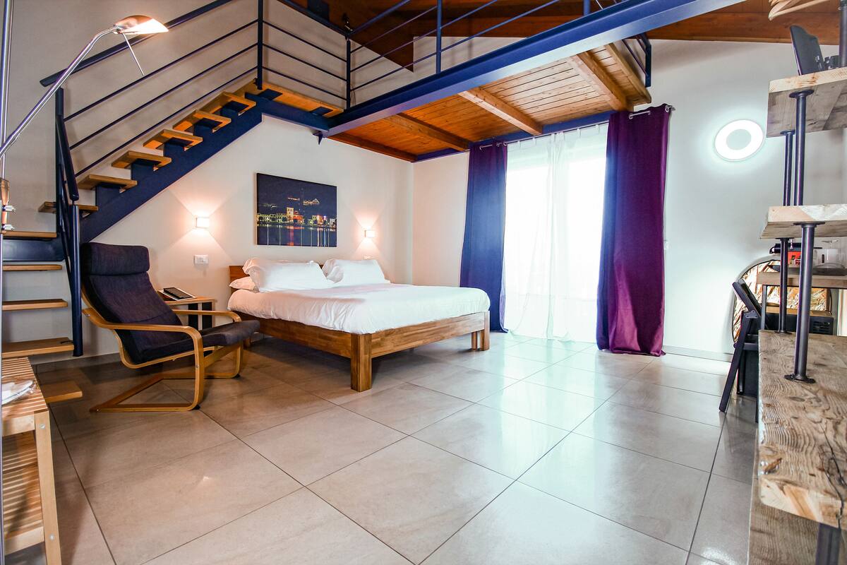 Quarto moderno com cama de madeira, uma cadeira, uma escrivaninha e uma escada.
