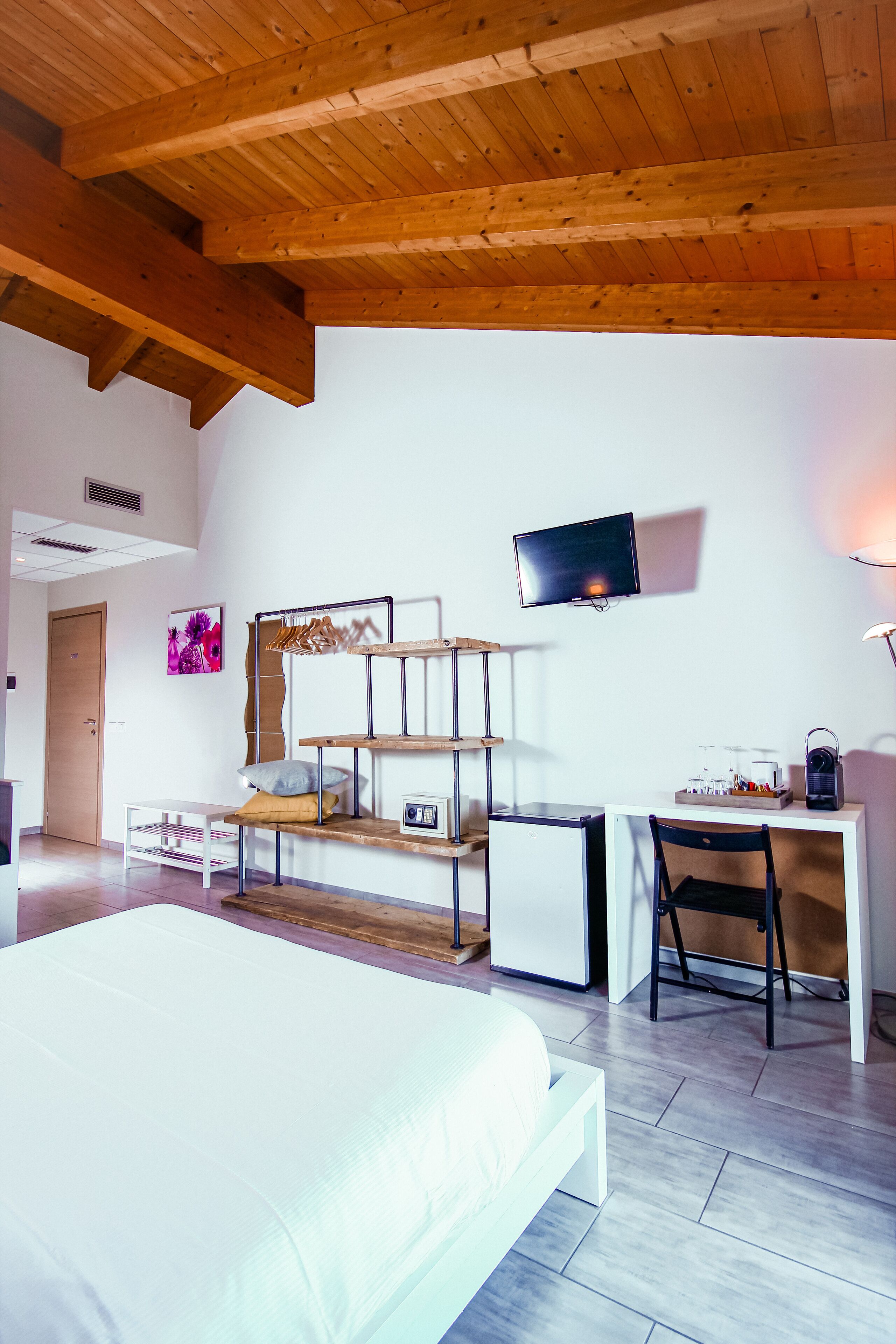 Ein modernes Schlafzimmer mit einem Bett, einem Schreibtisch, einem Sessel, einem Fernseher und einem Regal mit Dekoration.