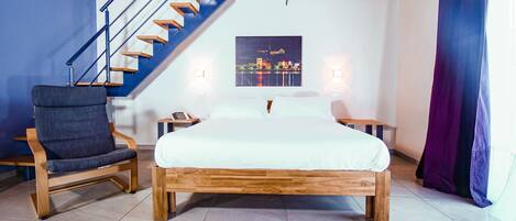 A bedroom with a wooden bed, a chair, a nightstand, and a staircase.