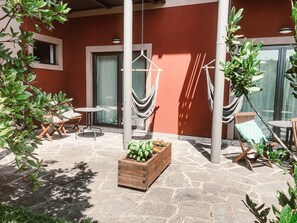 A patio with stone flooring, a wooden planter with plants, and two hammocks.
