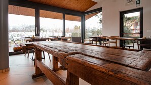 A spacious indoor area with large wooden tables and benches, large windows, and a view of the outdoors. - Agriturismo Il Cucchiaio di Legno (Orta San Giulio)