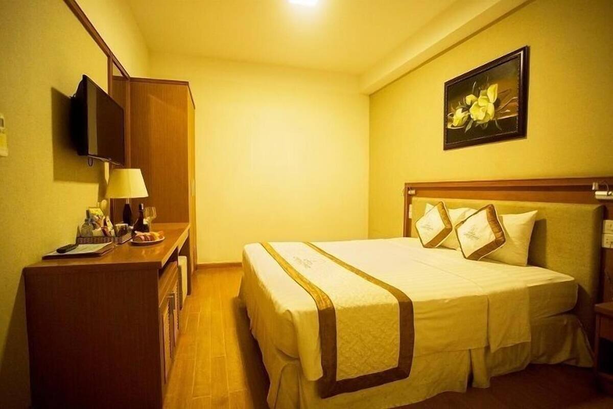 A hotel room with a bed, a desk with a lamp, a television, and a painting on the wall.