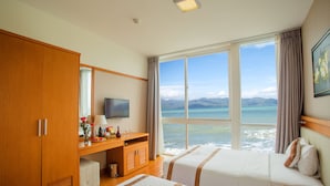 A hotel room with two beds, a wooden wardrobe, a television, and a view of the ocean. - Dendro Hotel (Nha Trang)