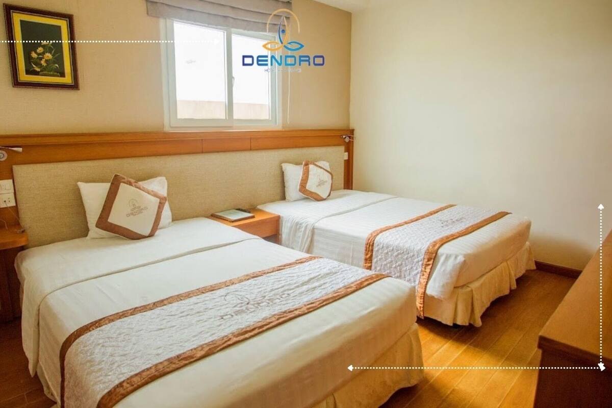 A hotel room with two beds, a wooden headboard, a bedside table with a phone, and a window with a view.
