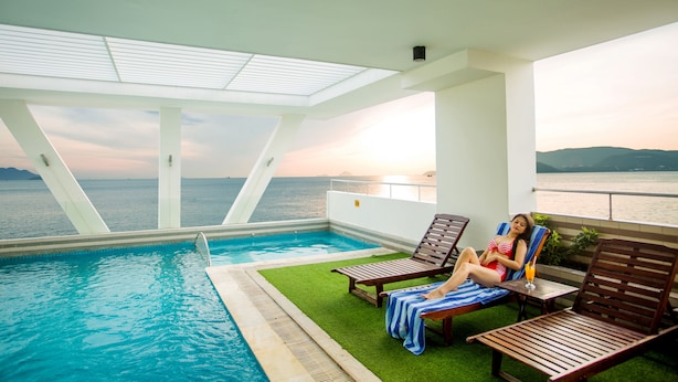 A pool area with a view of the sea, lounge chairs, and a person relaxing. - Dendro Hotel (Nha Trang)