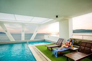 Area piscina con vista sul mare, sdraio e persona che si rilassa.
