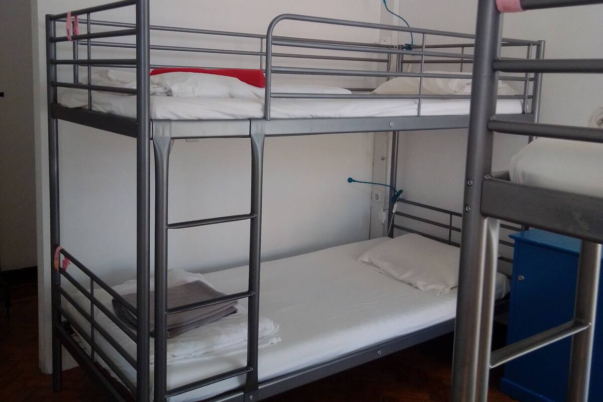 Una cama litera con barandillas metálicas y un armario azul.