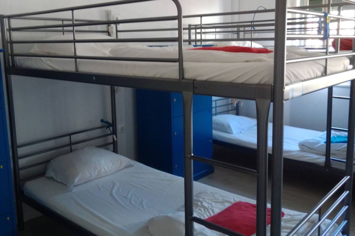 Habitación con literas, barandas de metal y ropa de cama blanca.