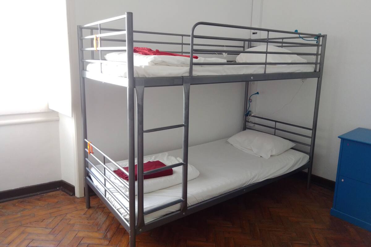 Una cama litera con barandillas de metal y ropa de cama blanca.