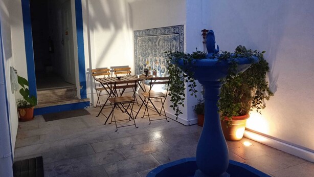 Ein Innenhof mit Esstisch, Stühlen, einer blauen Fontäne und Kübelpflanzen.