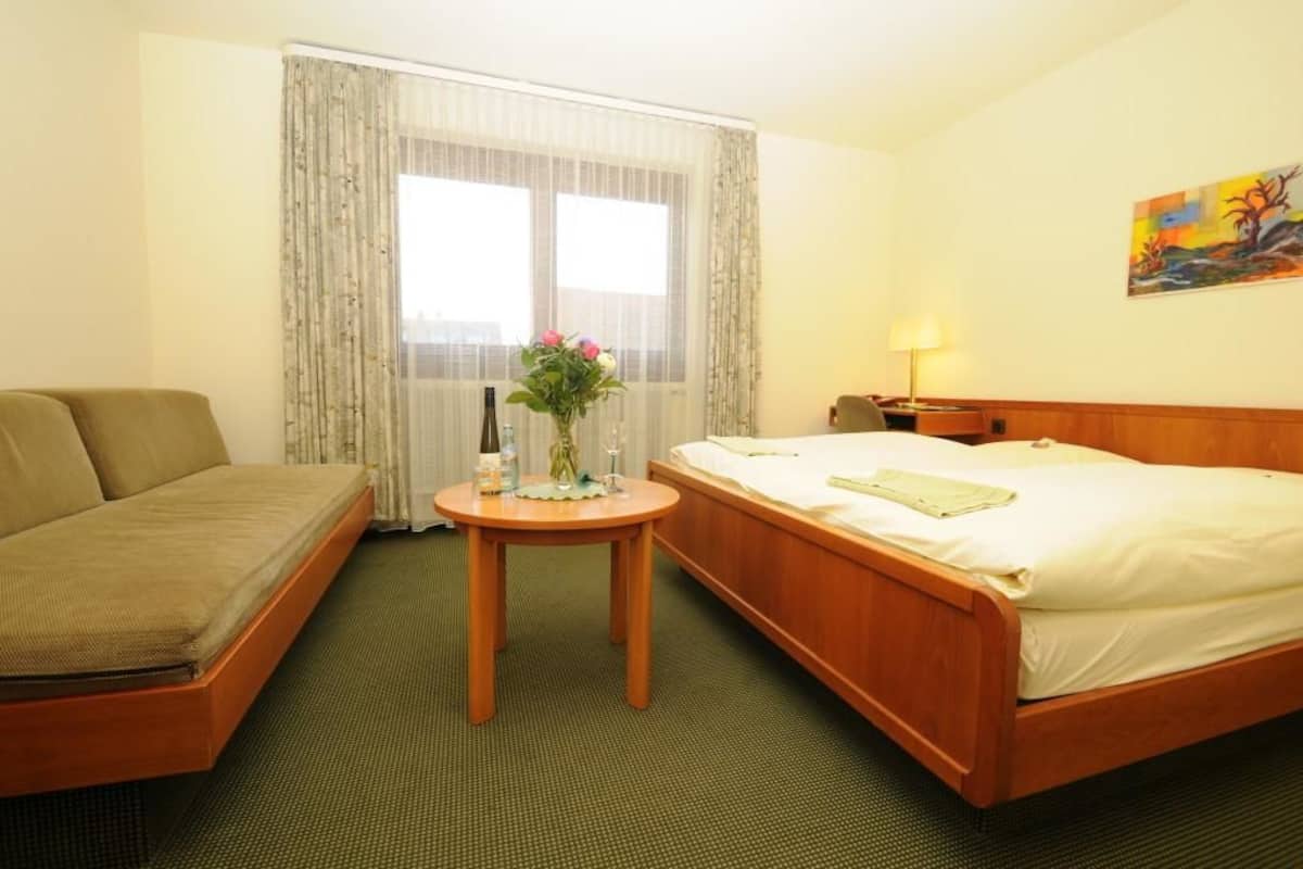 Et hotelværelse med en seng, en sofa, et lille bord med en blomstervase og et billede på væggen.