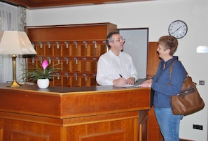 A reception desk with a wooden finish, a clock on the wall, and a potted plant. - Hotel Rheingauer Tor (Hochheim am Main)