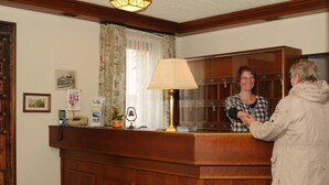 A reception desk with a wooden counter, a lamp, and a coat rack. - Hotel Rheingauer Tor (Hochheim am Main)