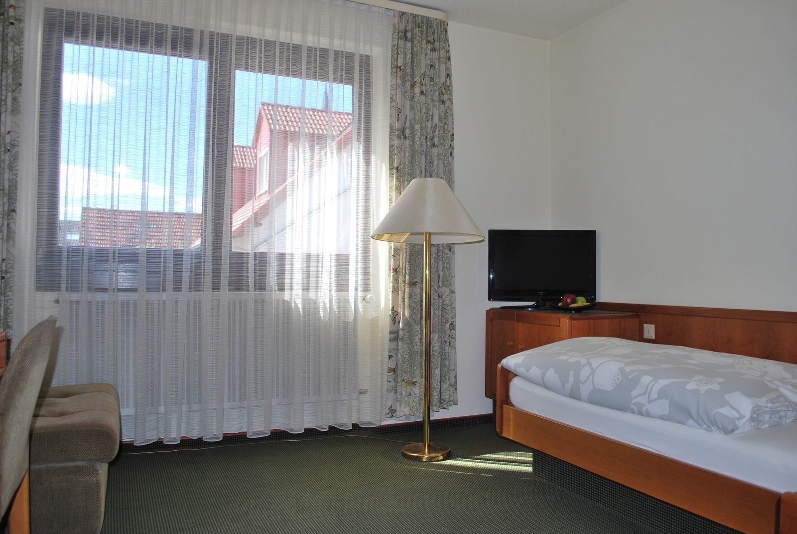 A hotel room with a bed, a TV, a lamp, and a window with curtains.