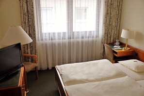 Una habitación de hotel con cama, escritorio, silla, televisor y ventana con cortinas.