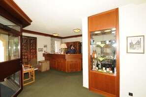 Un vestíbulo de hotel con una recepción, una zona de estar y un bar con botellas.