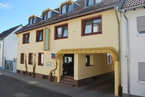Un hotel de dos pisos con fachada amarilla, múltiples ventanas y una pequeña entrada con escalones.