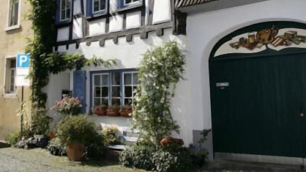 A traditional half-timbered building with a green garage door, potted plants, and a cobblestone street. - Hotel Rheingauer Tor (Hochheim am Main)