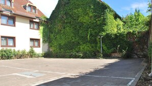 A parking lot with a paved walkway, a building with a red-tiled roof, and a large green wall covered in ivy. - Hotel Rheingauer Tor (Hochheim am Main)