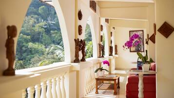 A balcony with a view of lush greenery, a wooden table with a vase of flowers, and a red sofa.