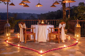 An outdoor dining area with a table set for two, surrounded by chairs, and a decorative flower path leading to the table. - Ayung Resort Ubud (Ubud)