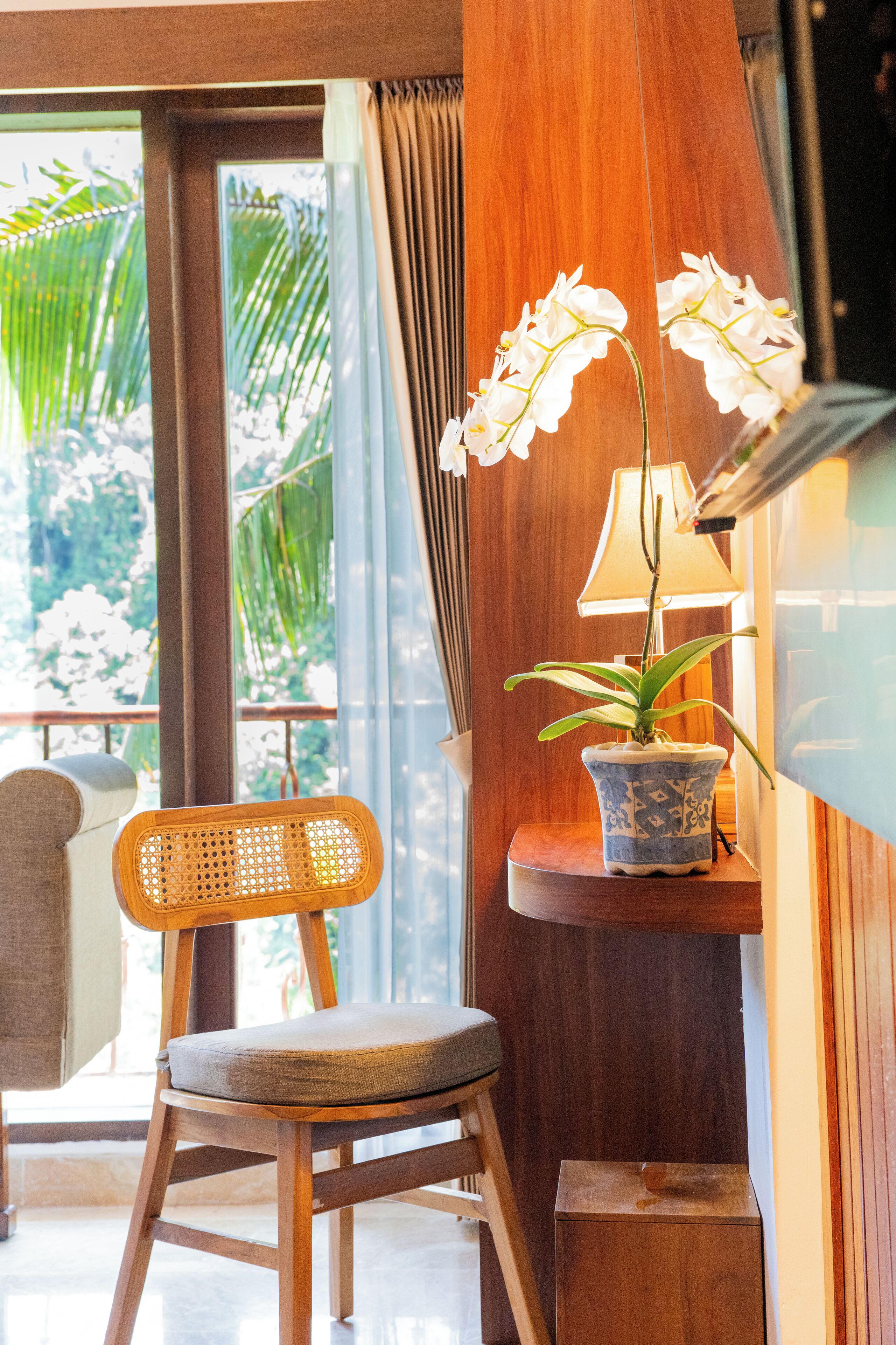 A wooden chair with a cushion, a potted orchid, and a lamp on a wooden table.