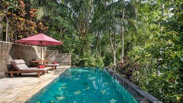 A swimming pool with lounge chairs and a red umbrella, surrounded by lush greenery.